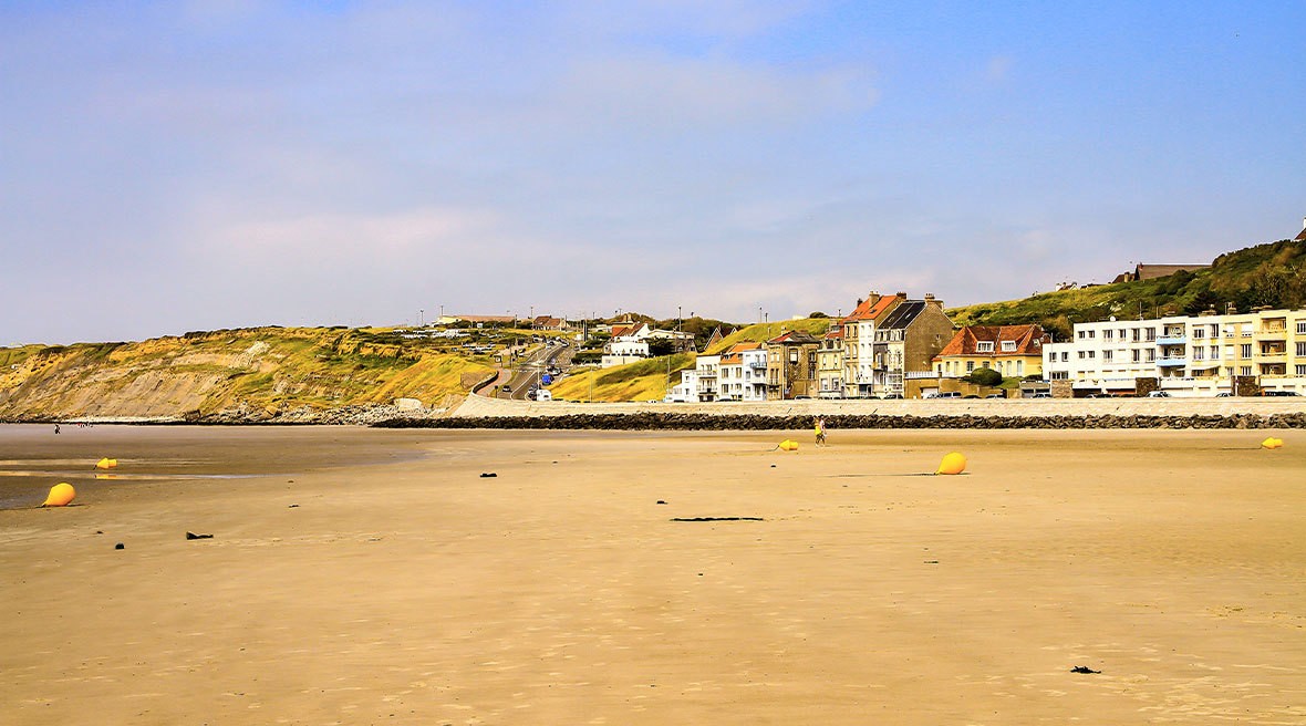 Golden beach with yellow buoys and buildings in the distance, under a blue sky