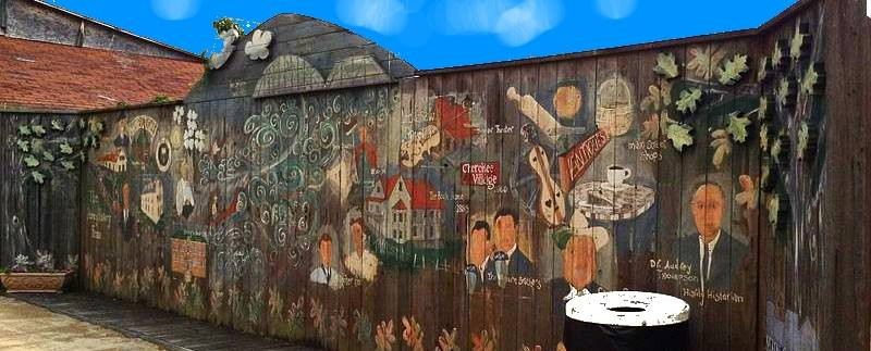 A colorful mural on a wooden fence featuring various scenes, characters, and nature elements against a blue sky.
