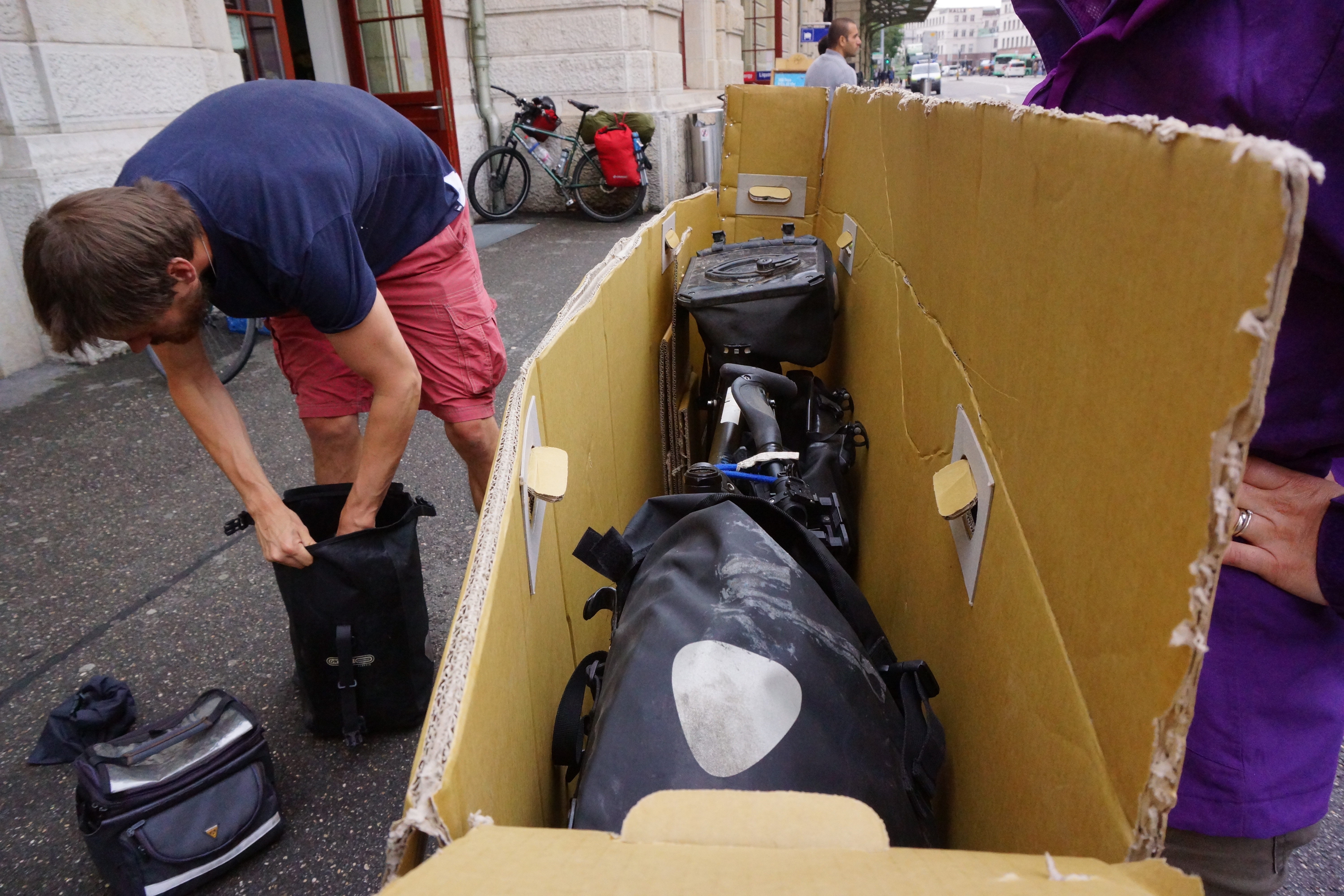 Packing a touring bike into an open cardboard bike box, complete with panniers.