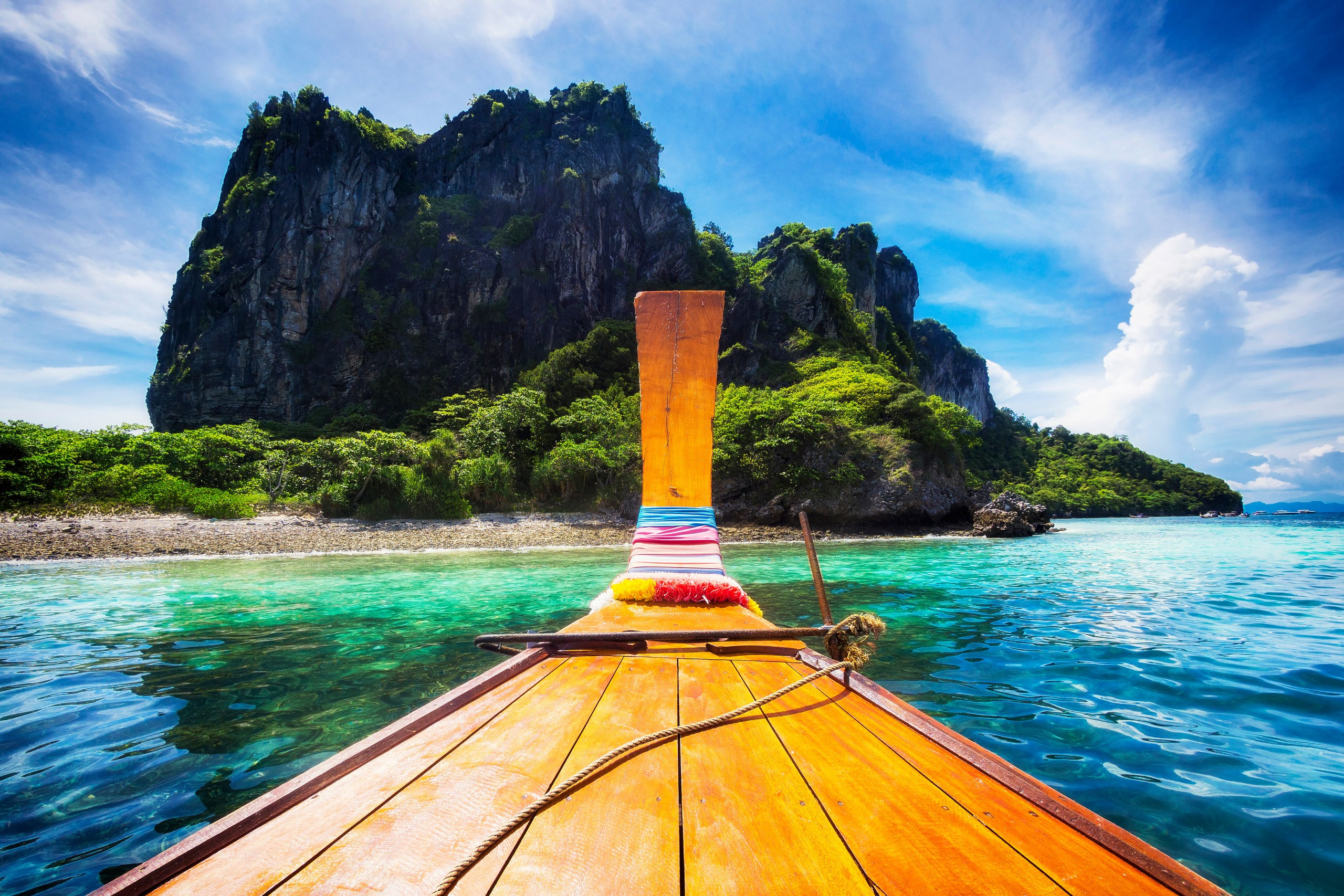 A traditional long-tail boat approaching Maya Bay beach on Koh Phi Phi, Thailand, under a bright sky