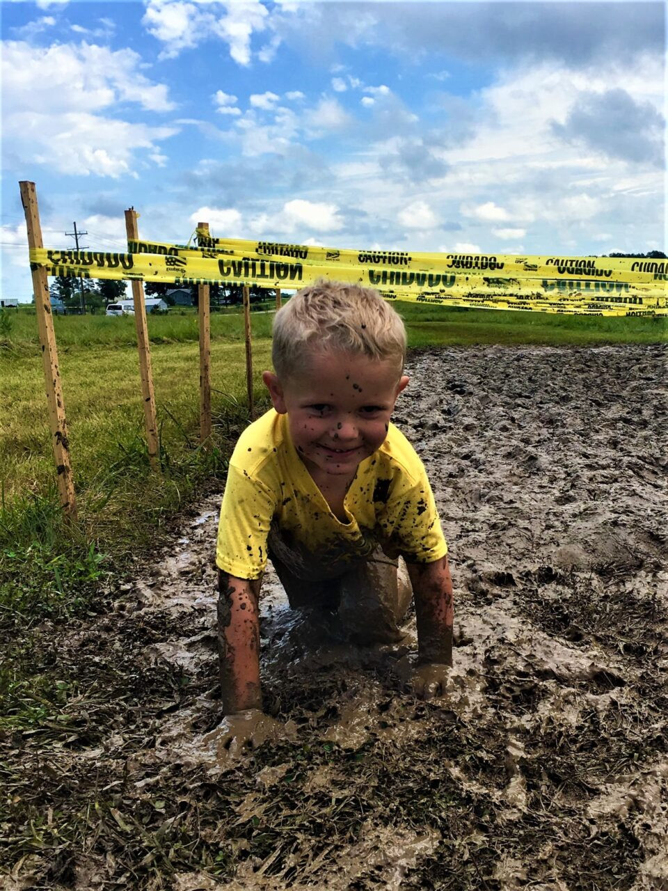 A photograph of a smiling child crawling through the mud, participating in the 
