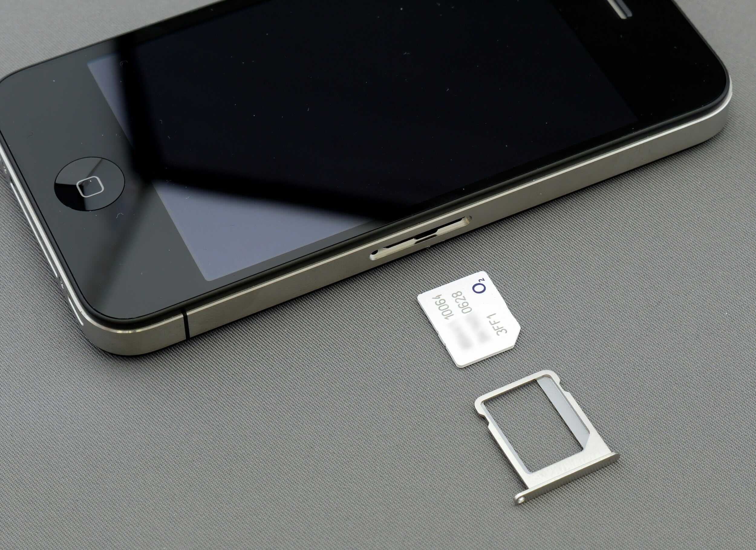 A smartphone next to a SIM card and its metal tray, placed on a gray surface.
