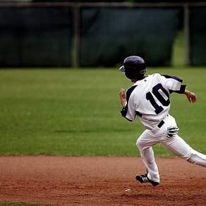 A baseball player running on a baseball field in a black and white uniform with a helmet on.
