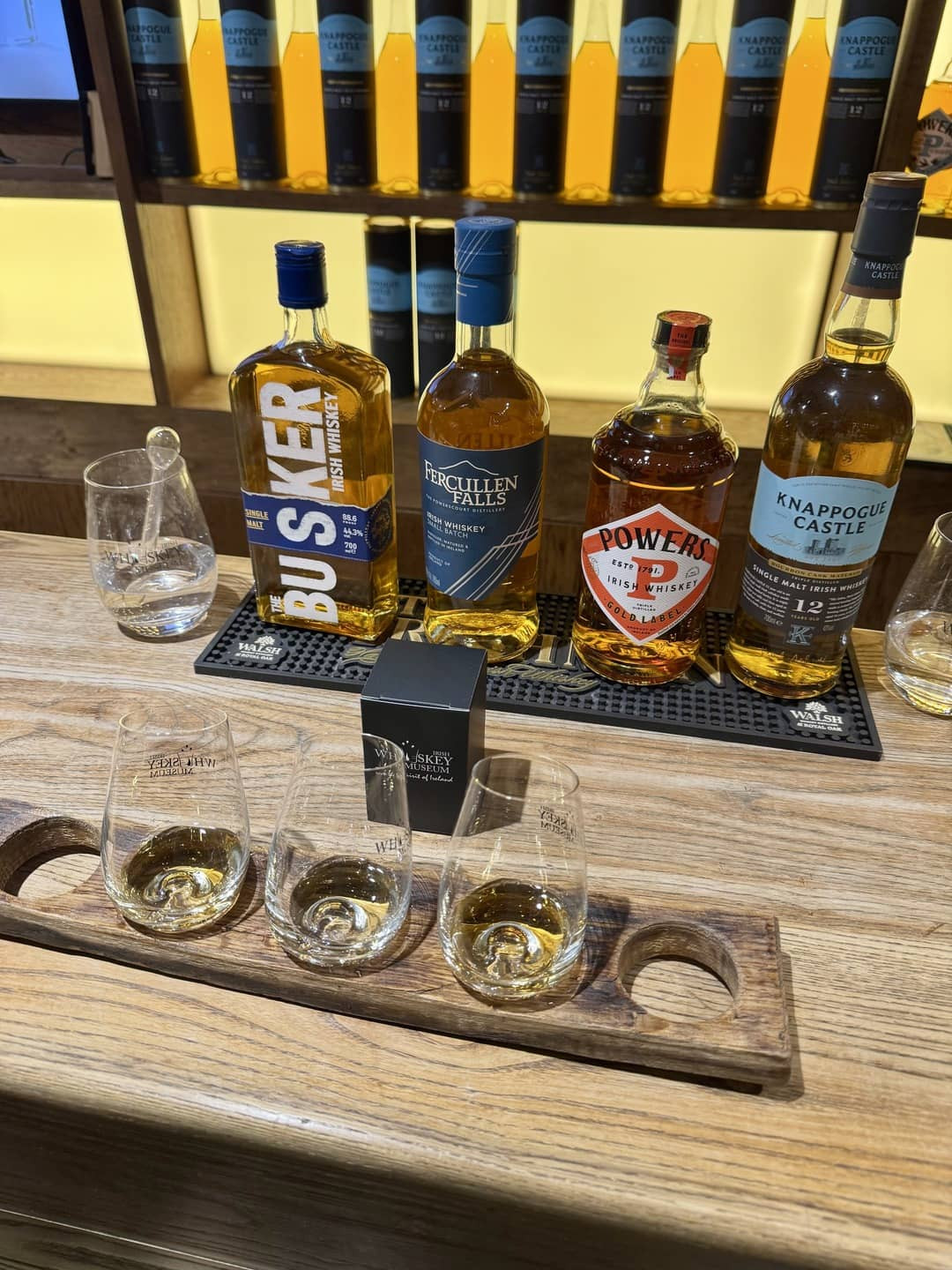 A wooden tray displaying various glasses and bottles at the Irish Whiskey Museum, showcasing a selection of fine spirits and the rich heritage of Irish whiskey.