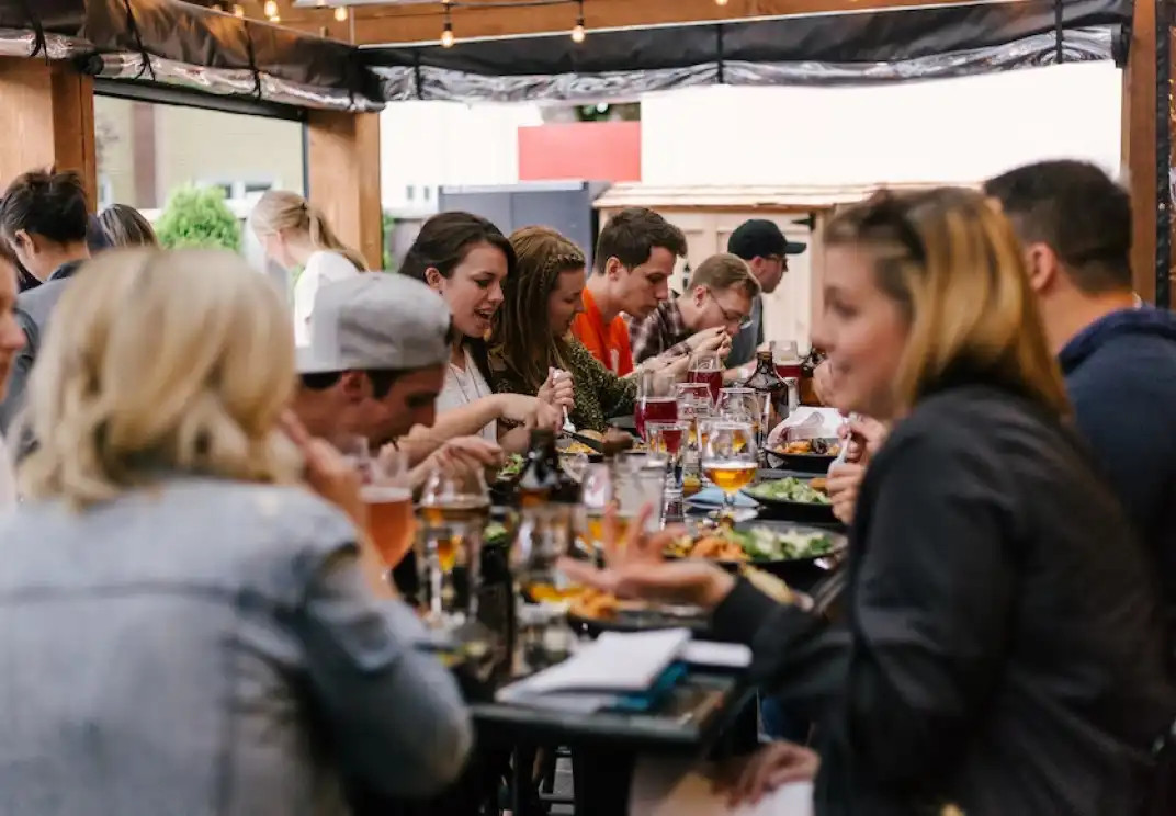 Group of friends enjoying meal together at communal dining table with drinks