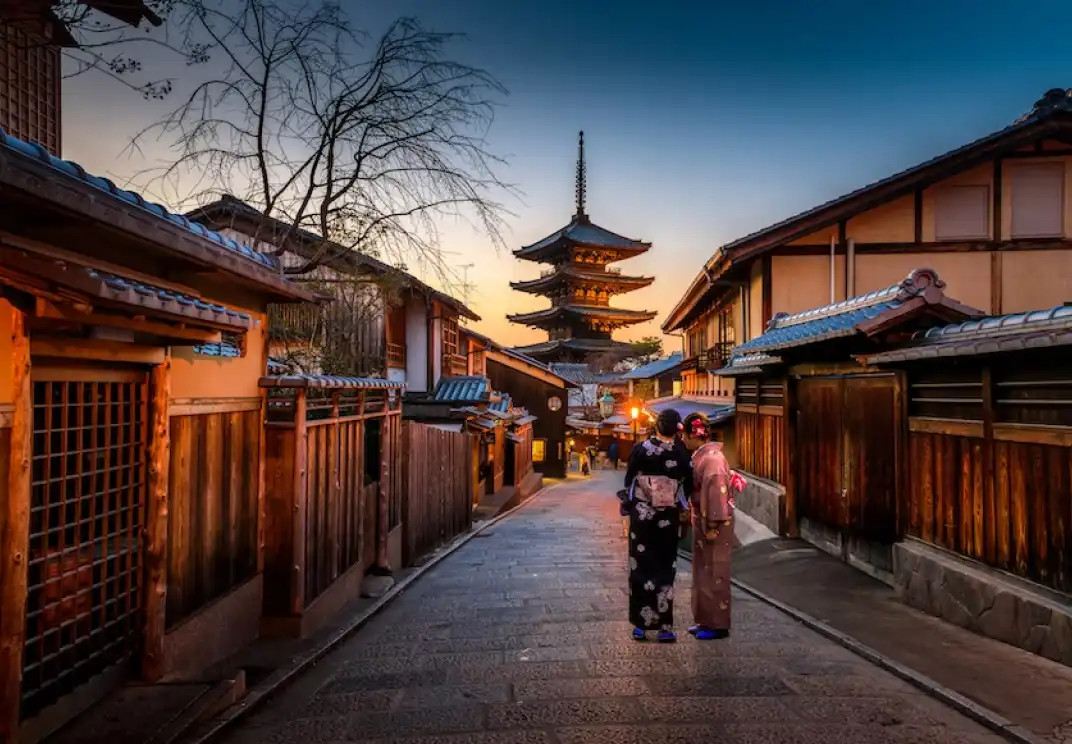 Traditional Japanese street in Kyoto with pagoda at sunset, two people in kimonos