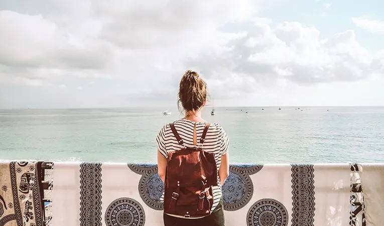 woman in black and white striped shirt with bun and red backpack looking at ocean
