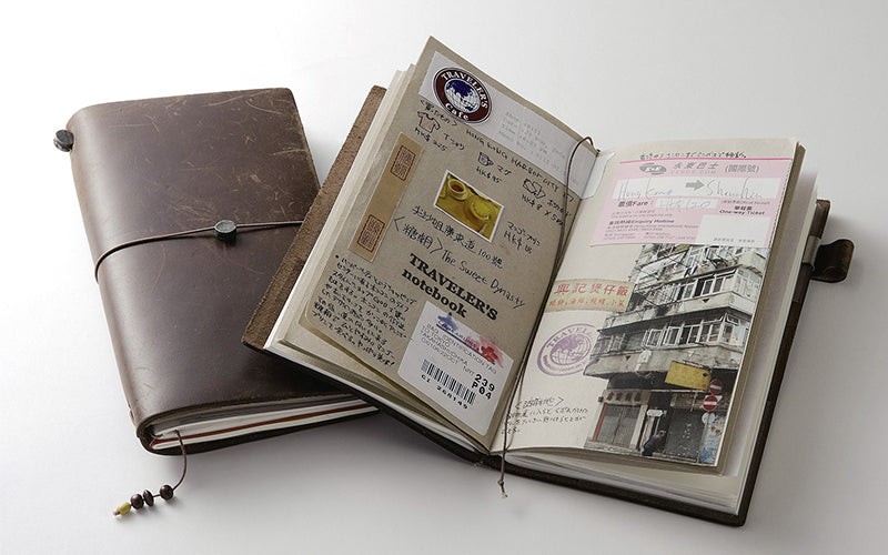 Traveler's notebook with leather cover, elastic band closure, and various notebook inserts displayed on a wooden surface