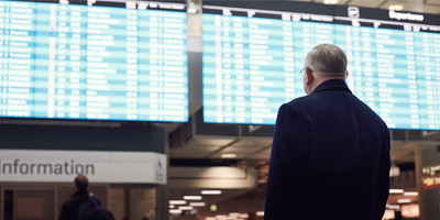 Man looking at arrivals and departures board in an airport. This image represents the challenges and planning required for traveling with dementia.