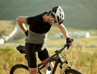 Man holding his lower back in pain while standing next to his bicycle, illustrating how physical activities without proper preparation can lead to back issues.