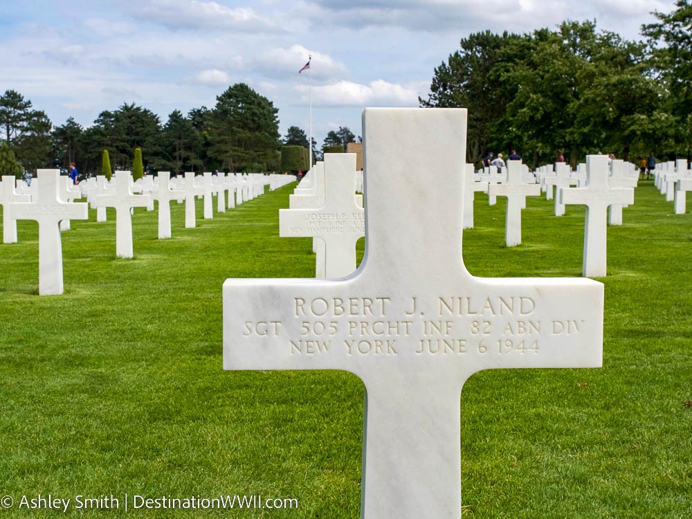 white marble cross-shaped headstone with Robert J. Niland on it