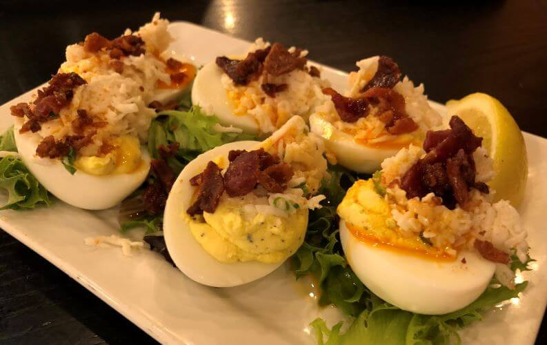 six deviled eggs with bits of bacon bits and a slice of lemon