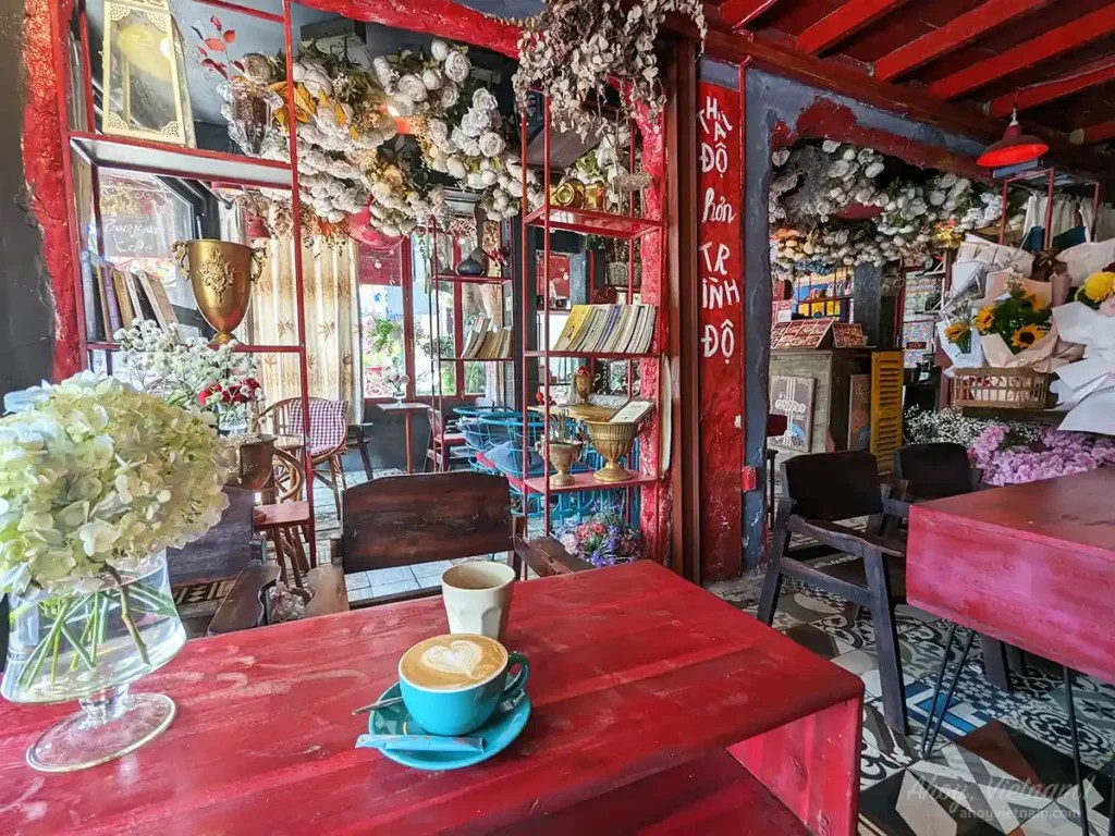 Hot coffee inside Bonjour Cafe The Art in Thao Dien, one of the best areas to stay in Ho Chi Minh City, showing numerous pink and red decorations and flowers adorning the walls and ceiling