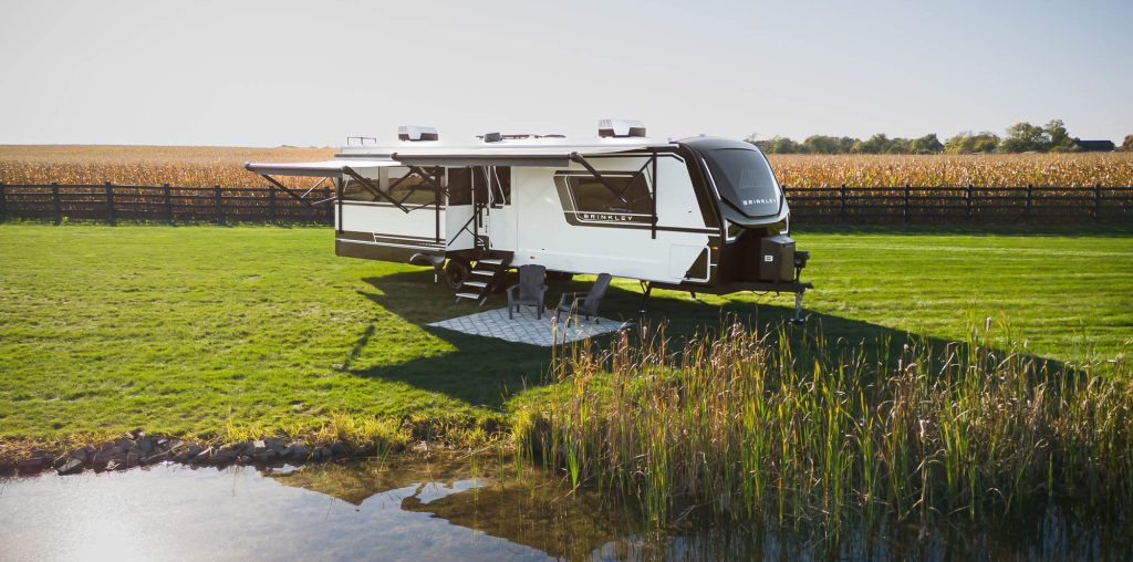 A Brinkley RV luxury travel trailer set up by a pond, offering premium features and high-end finishes