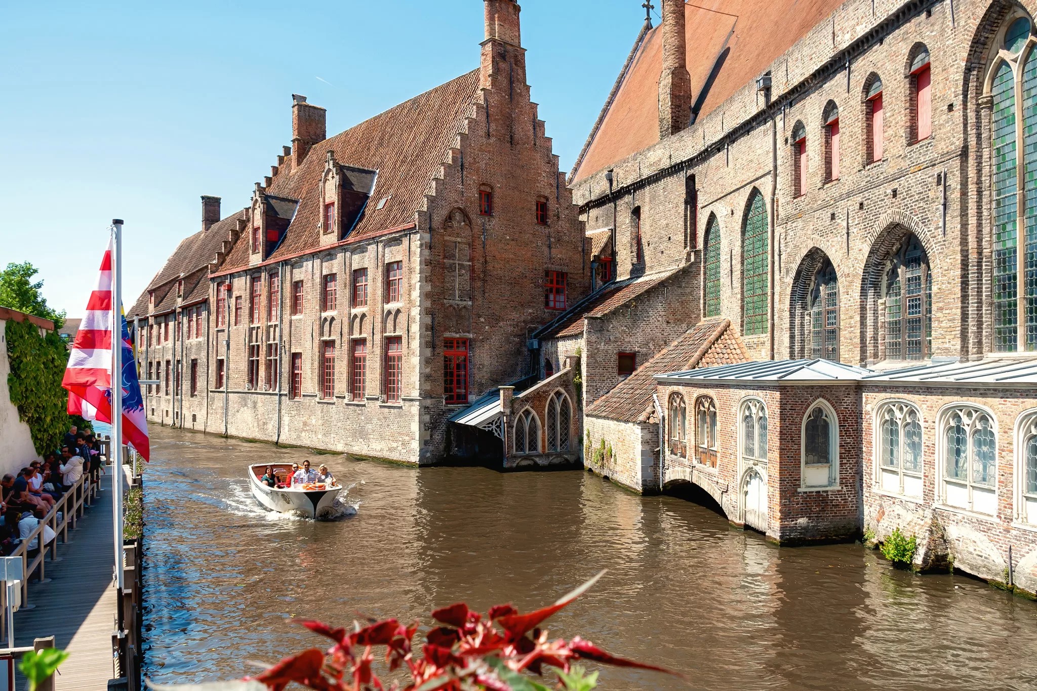Canal tour boat in Bruges cruises along the water with historical buildings in the background.