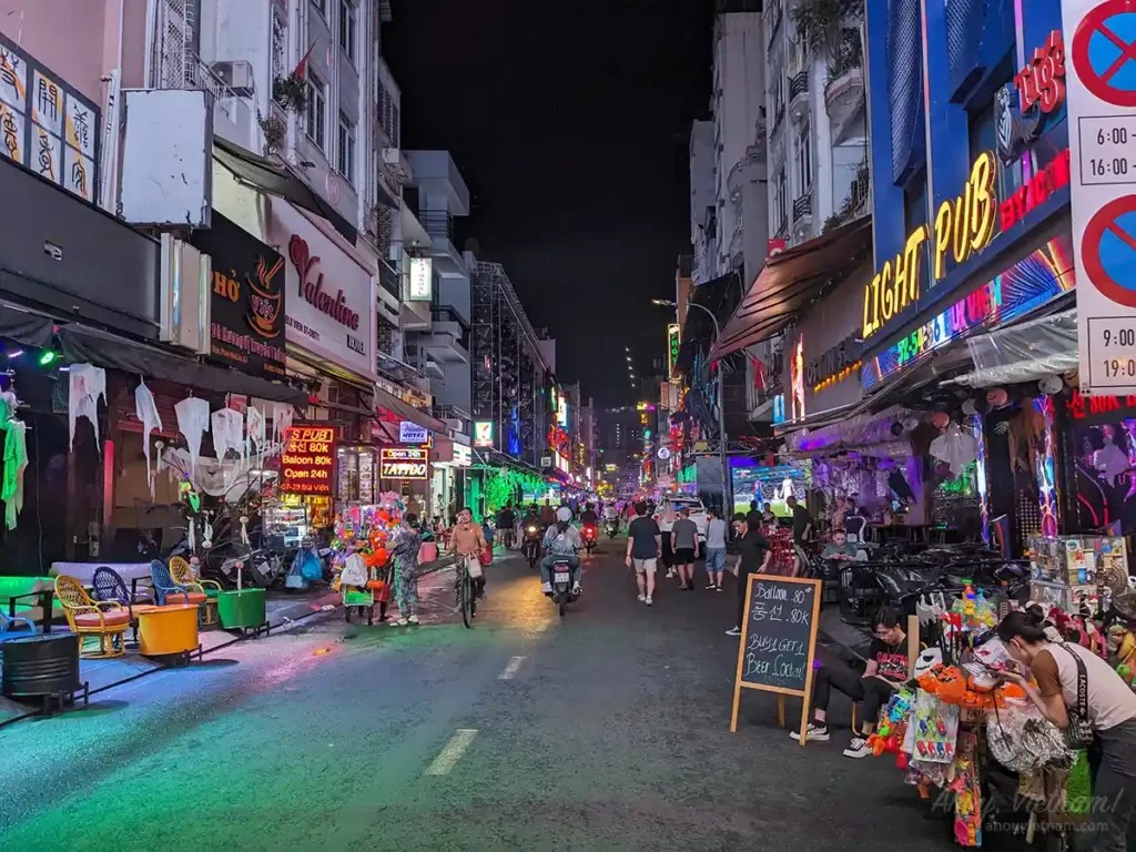 Bui Vien Walking Street, one of the best areas to stay in Ho Chi Minh City, at night, with neon lights, bars, restaurants, tourists, display signs, and locals.