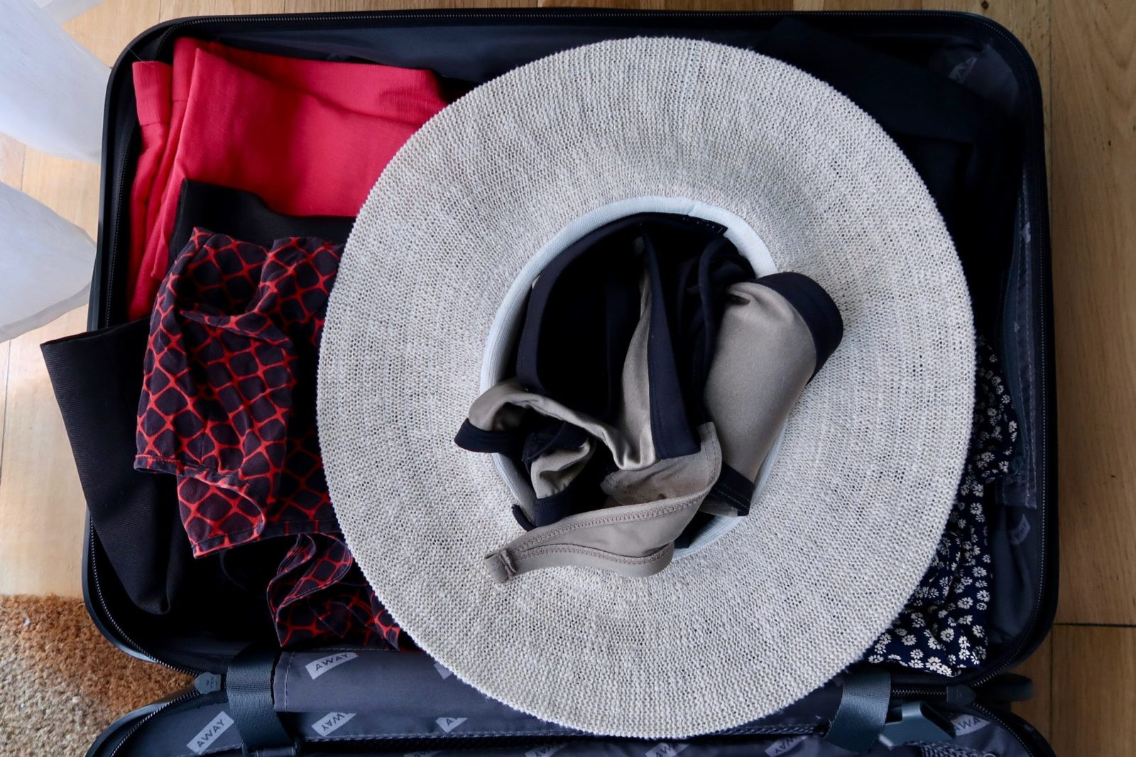 Straw hat packed upside down in a suitcase with clothing stuffed around it