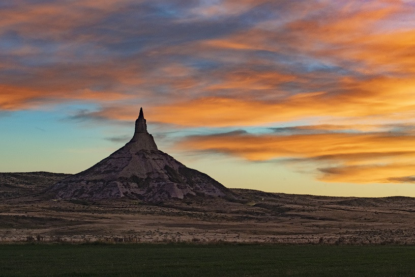 Chimney Rock Alt Text: Chimney Rock, a towering natural sandstone formation in Nebraska, illuminated by sunlight against a clear blue sky, showcasing its historical significance as a landmark for westward travelers.