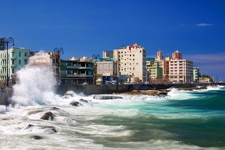 Pastel-colored buildings lining the Malecon in Havana, Cuba, with vintage cars in the foreground