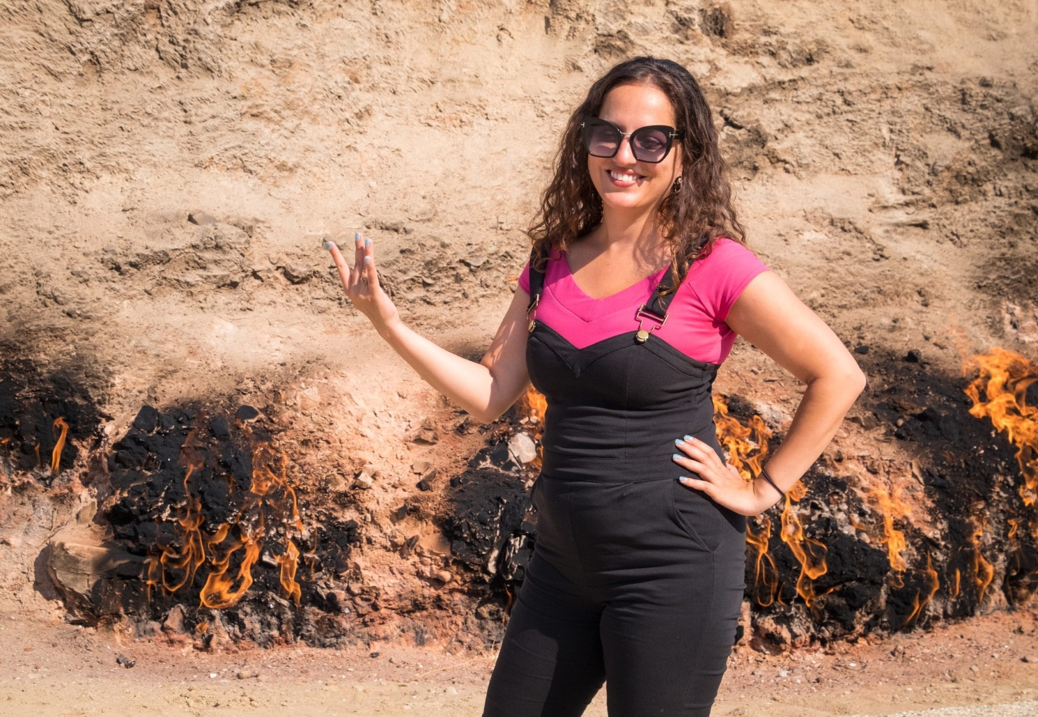 Kate standing in front of the burning ground at Yanar Dag in Azerbaijan, creating a finger flame gesture, capturing the essence of the Land of Fire