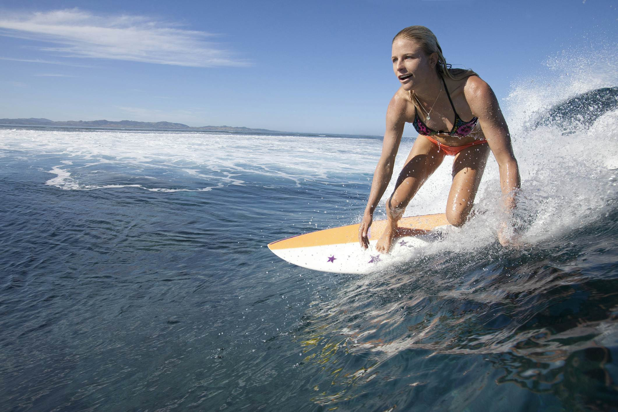 A woman in a bikini rides a surfboard on a large wave