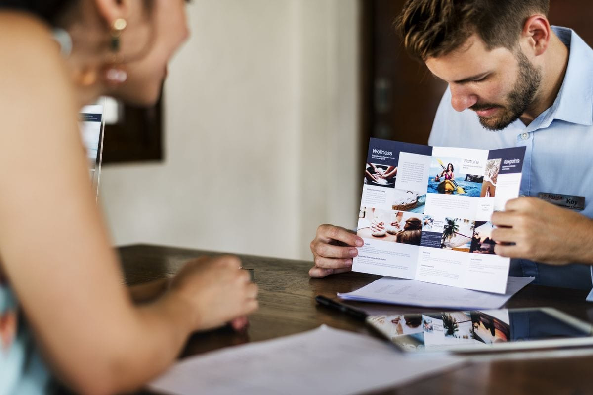 Man showing woman across a desk a pamphlet. Get front desk work abroad