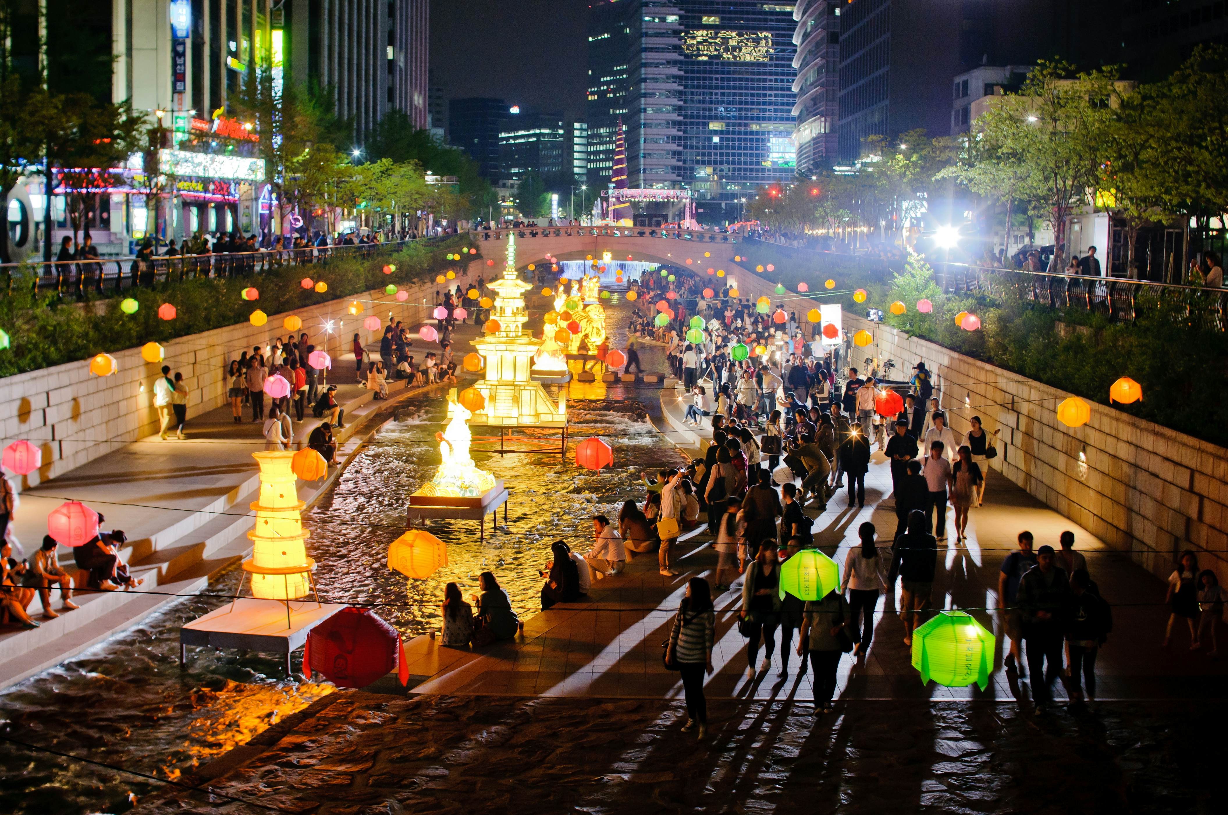People walk by lanterns and lit-up sculptures that decorate a waterway