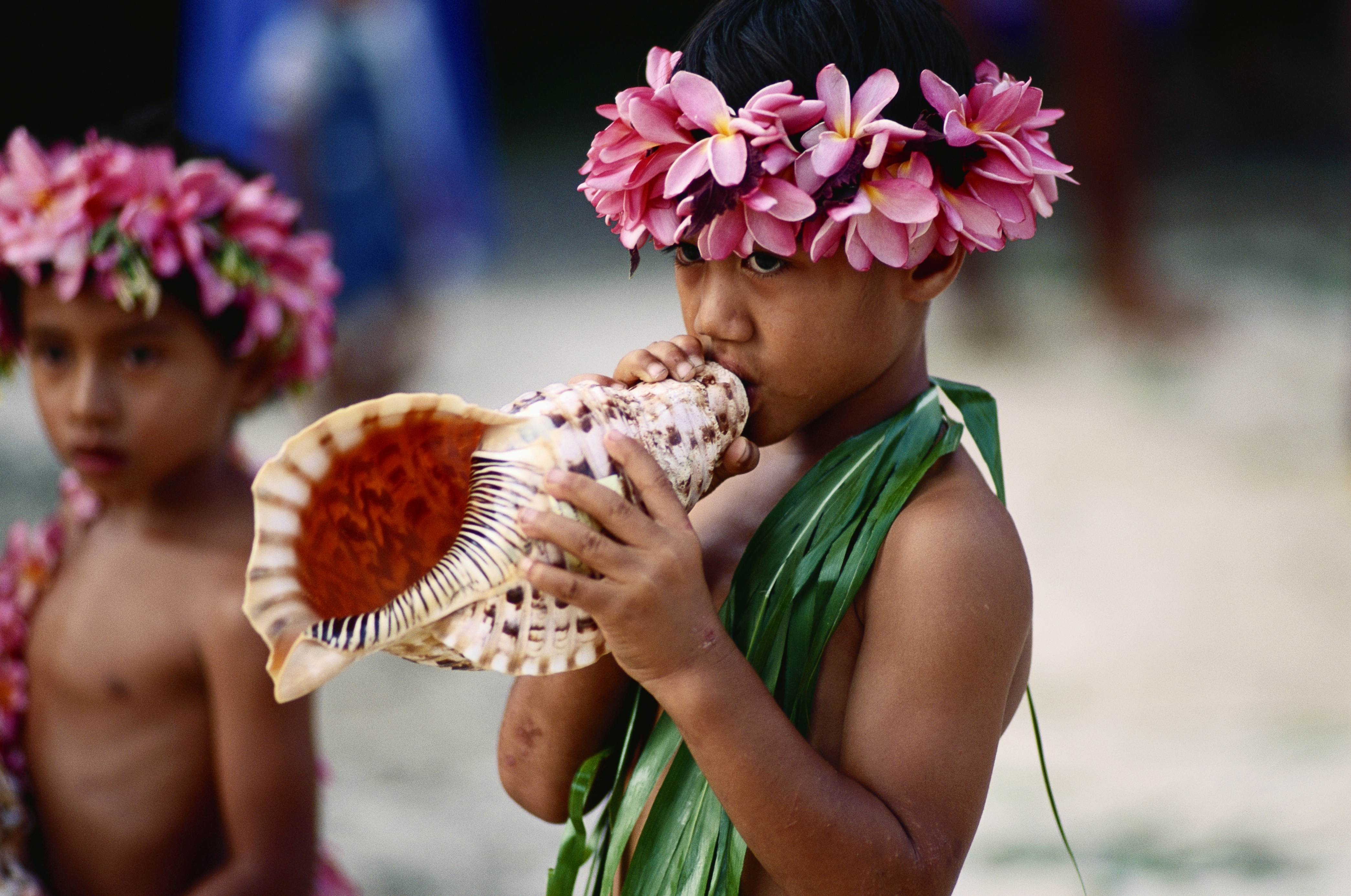 A child blows a conch-shell greeting in the Cook Islands