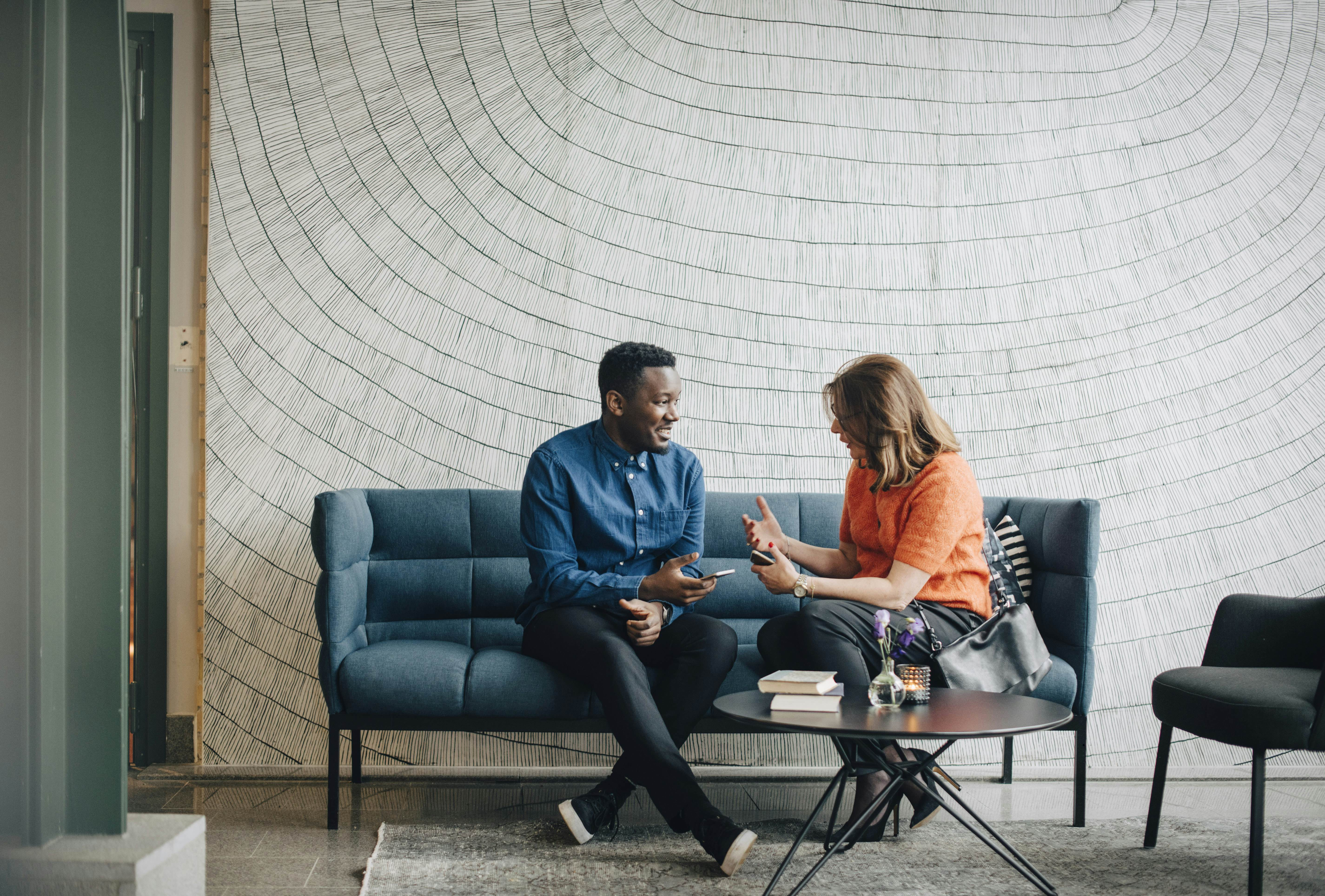 A businessman and a woman engage in conversation while seated on a couch against a wall at a conference