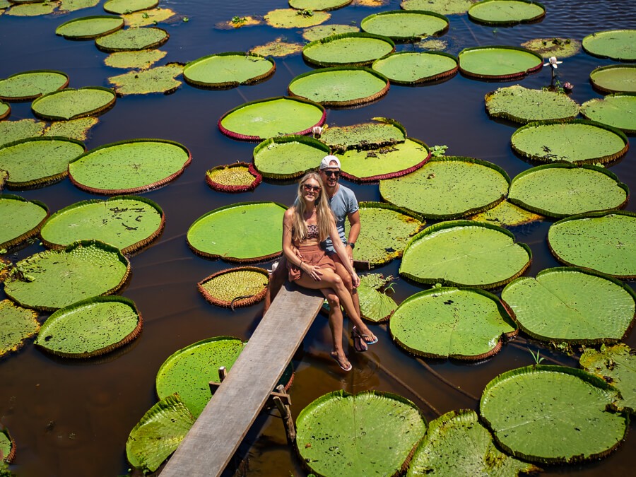 Me and my boyfriend sitting on a dock surrounded by giant water lilies, one of the best places to visit in the Amazon rainforest in Brazil