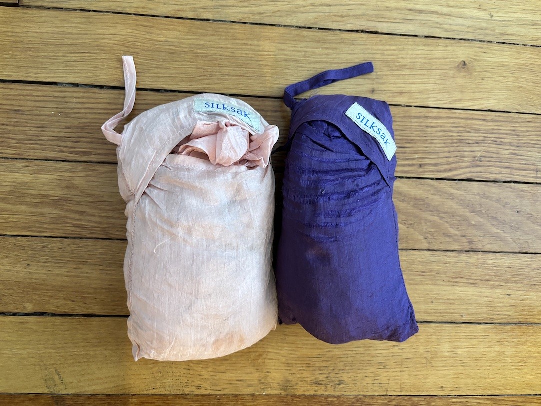 Two SilkSak sleeping bag liners are folded up and photographed on a hardwood floor