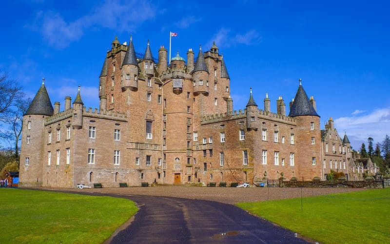 Glamis Castle under a sunny sky, its historic facade and towering turrets hinting at the dark tales and ghostly legends that have made it a renowned destination for dark tourism.
