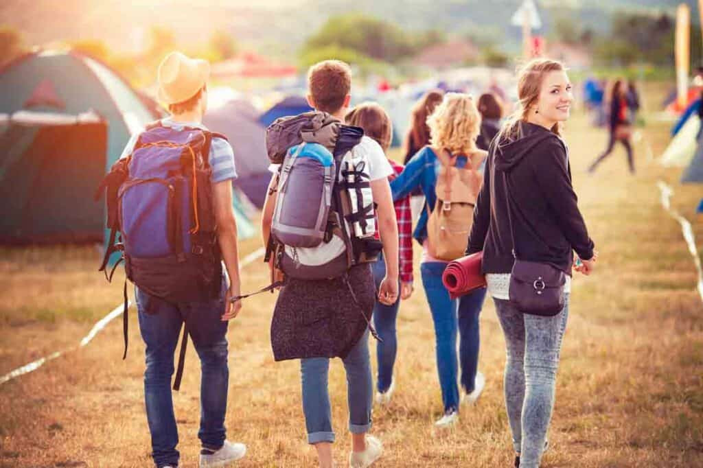 group of young people with backpacks walking towards campsites.