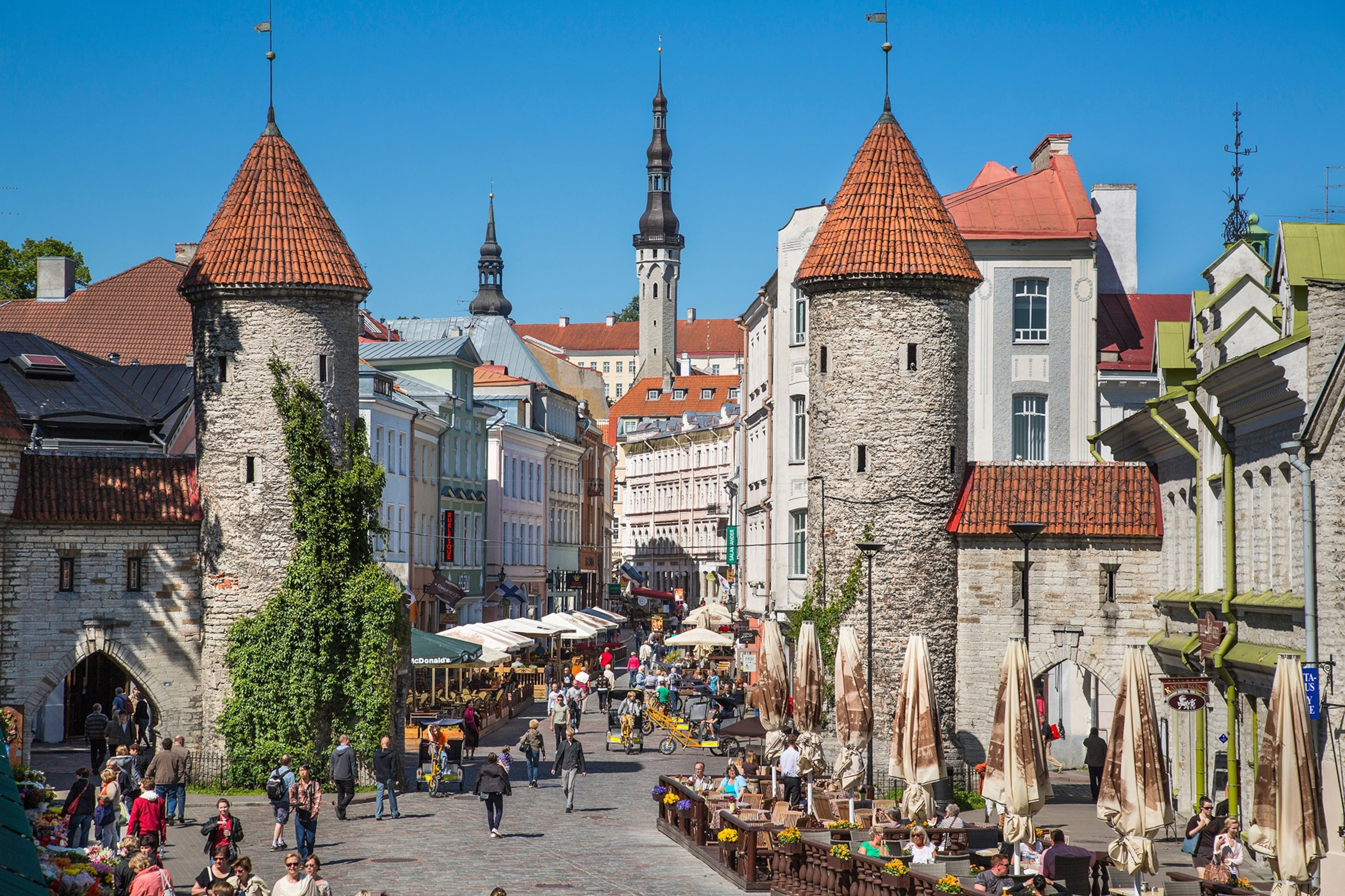 Two towers frame the road with people walking out and about in Tallinn Old Town.