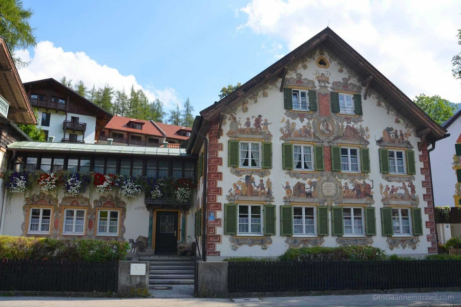 A building in Oberammergau, Germany is white, with green shutters, and elaborate murals telling the story of Hansel and Gretel.
