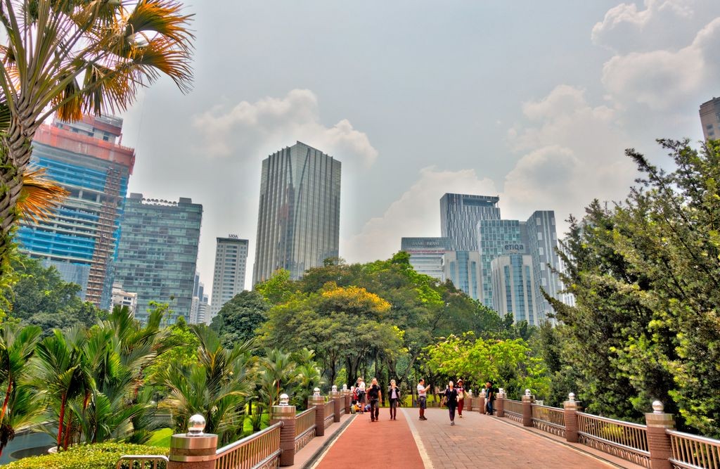 People on a walkway surrounded by trees with buildings in the background in Malaysia.