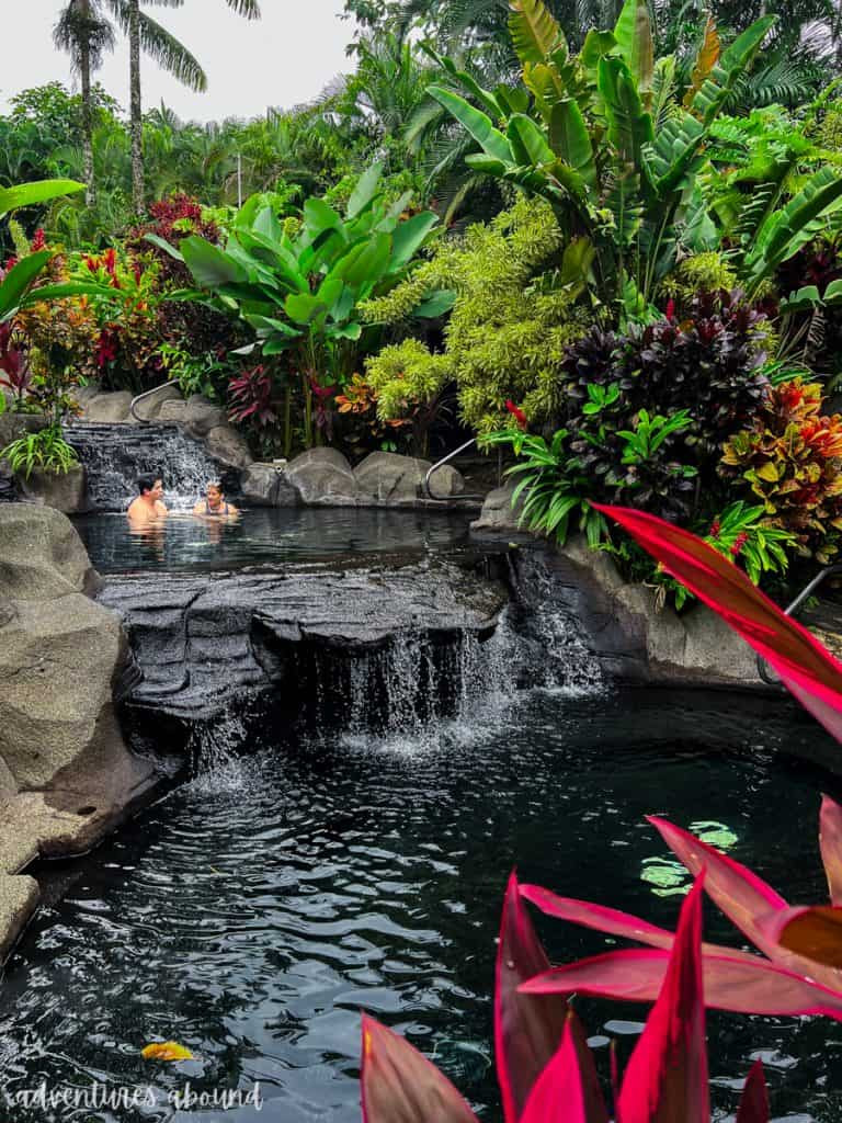 Two people sitting in a hot spring pool in La Fortuna, surrounded by lush nature in Costa Rica