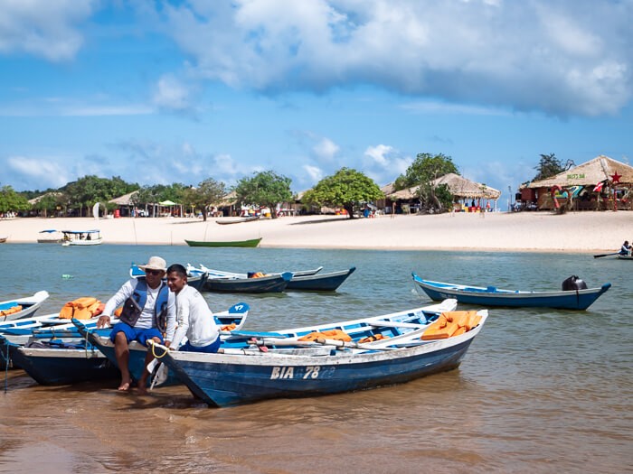 two men sitting on wooden boats in front of a white sand beach in Alter do Chão
