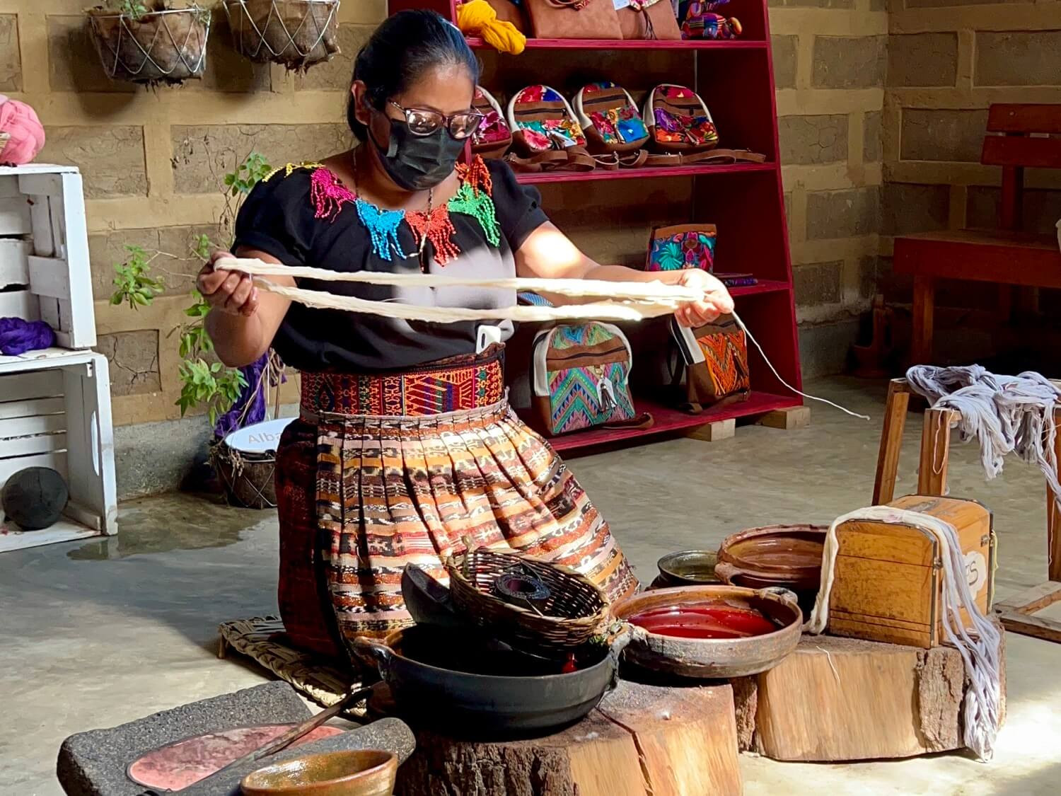 Guatemalan woman in black shirt with colored collar, belt and skirt demonstrating dying process of cotton with natural dyes in bowls