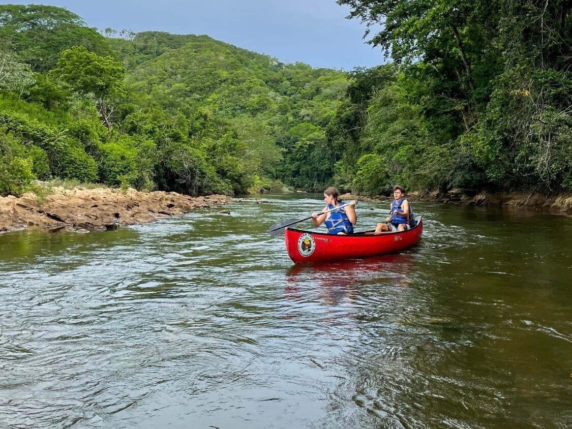 Two kids in red canoe paddling in river