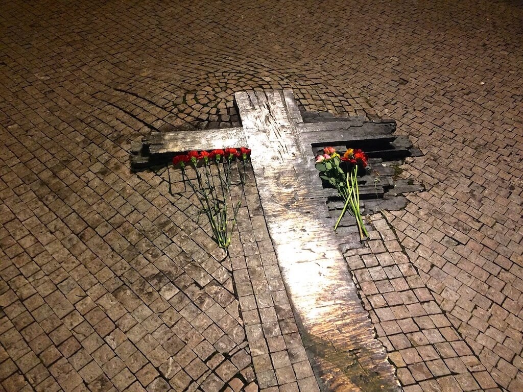 Metal cross melding into the ground with flowers. Memorial for Jan Palach and Jan Zajic on Wenceslas Square, Prague