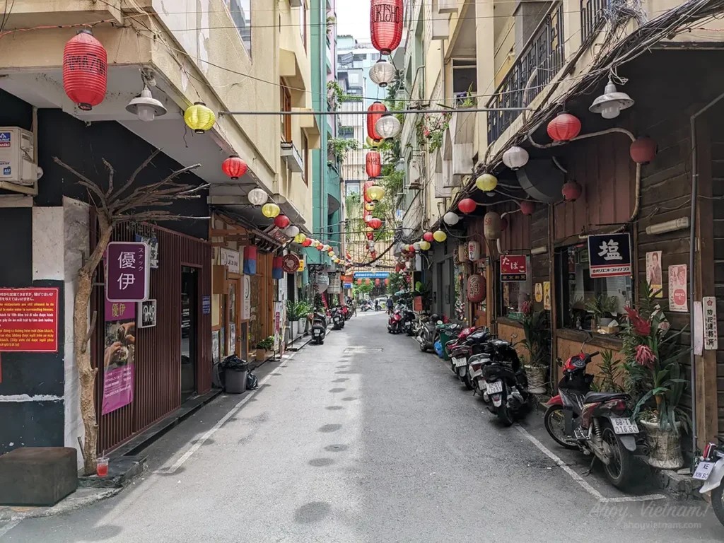 The entrance alley of Japan Town in District 1, Ho Chi Minh City, shows Japanese lanterns, restaurants, motorbikes, and tourists. 