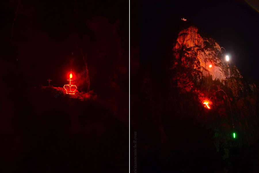 The Kofel, a mountain peak in Oberammergau, Germany, is illuminated with flares and flames. A symbol of a cross and royal crown are on fire. It is nighttime and the sky is dark. The event is an annual bonfire celebrating the eve of the birthday of the Bavarian King Ludwig II.