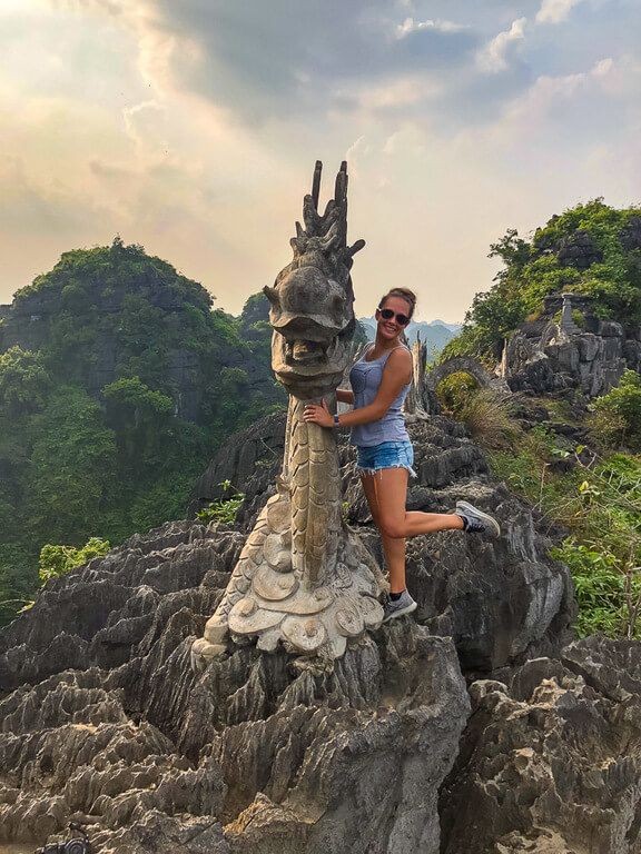 Woman posing for a photo on top of the stone dragon at Mua Cave viewpoint, capturing the essence of Ninh Binh