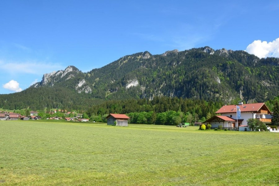 A forested mountain towers over a Bavarian house and wooden barn in the village of Oberammergau, Germany.
