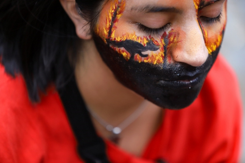 A woman wearing face paint at a protest over Australia's bushfires crisis, highlighting changing public attitudes and the demand for climate action and sustainable travel