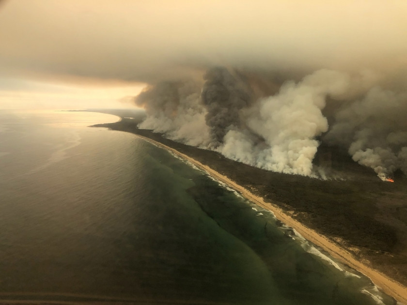 Thick plumes of smoke rising from bushfires in East Gippsland, Victoria, illustrating the climate feedback loop and its impact on environmental disasters and tourism