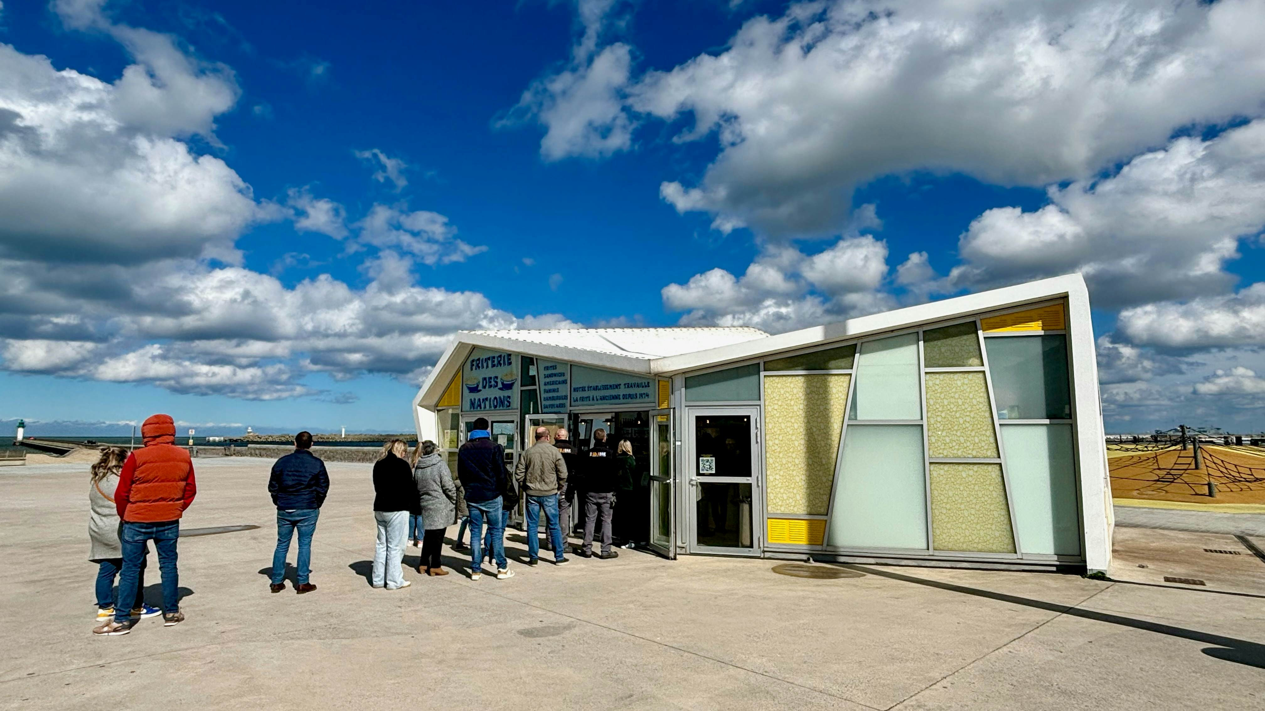 A line of people eagerly waits outside a seaside kiosk for a taste of the famous Friterie des Nations fries