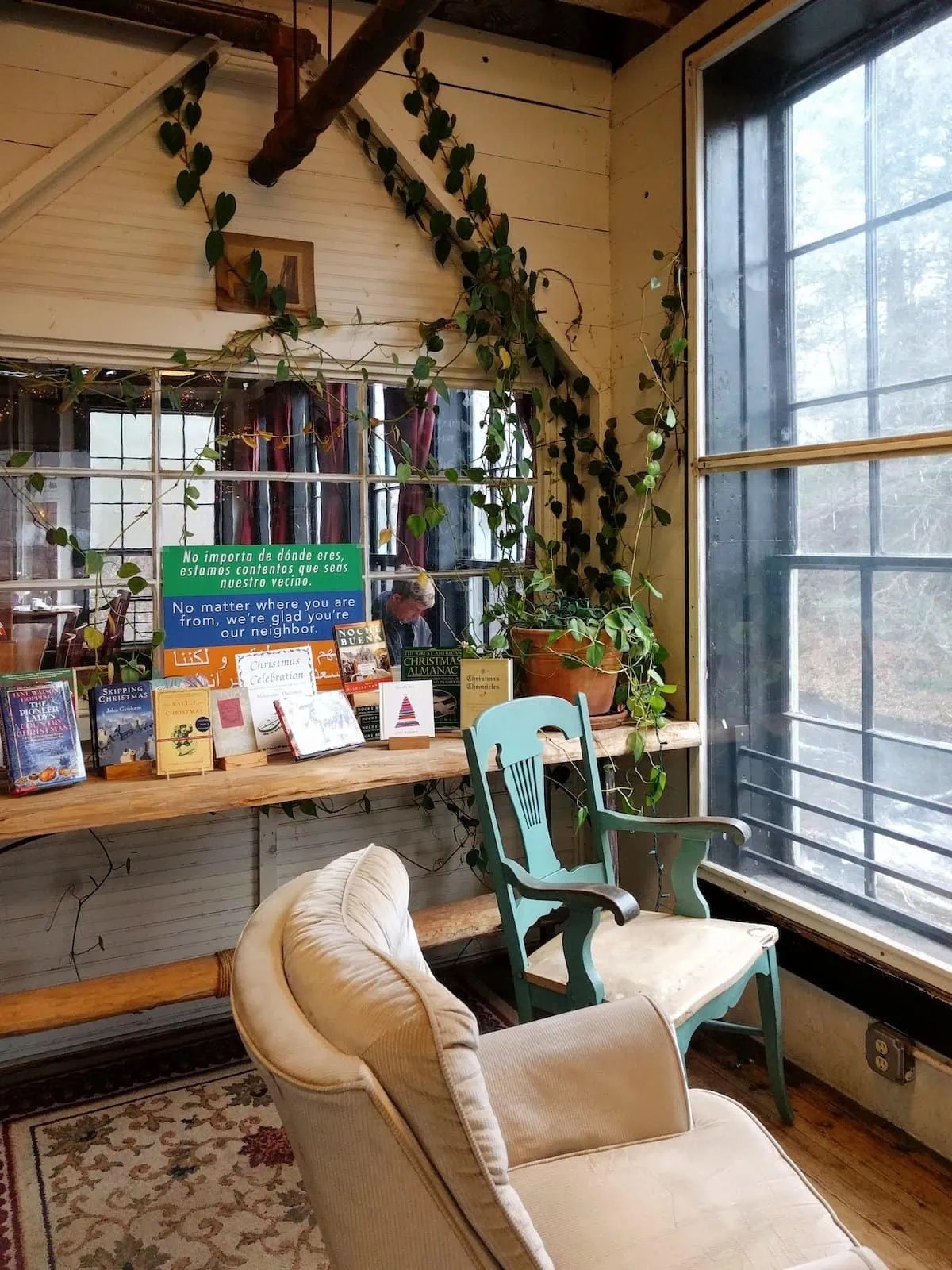 Cozy nook in the Montague Bookmill with plants, seating, and a window overlooking the river