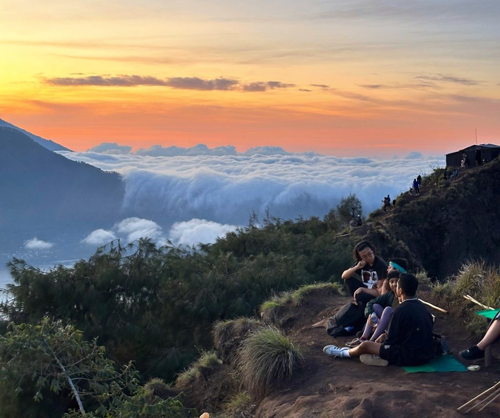 Tourists enjoying the breathtaking sunrise view from Mount Batur, with a sea of clouds rolling below.